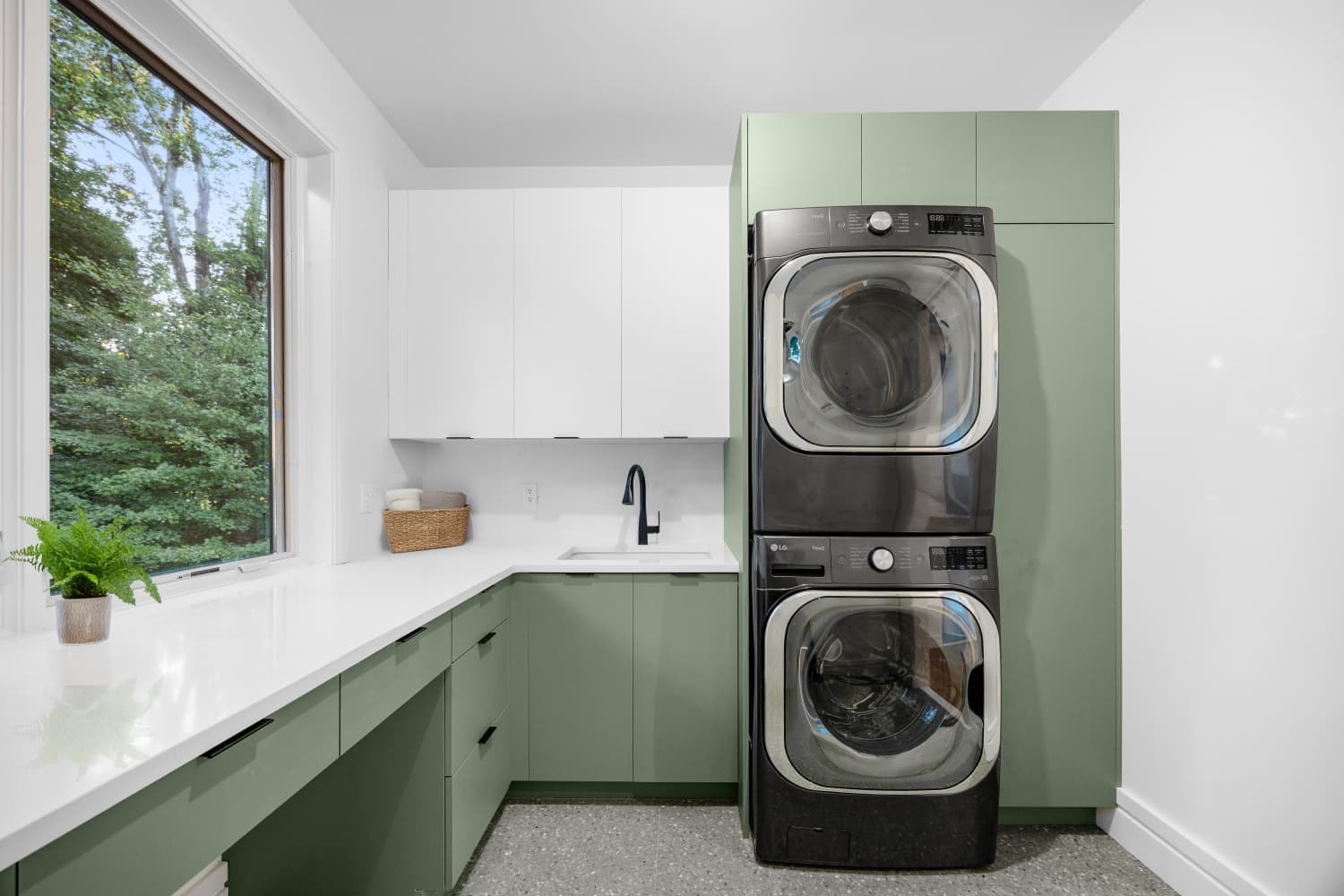 Custom laundry room with sage green cabinets and a stacked washer and dryer