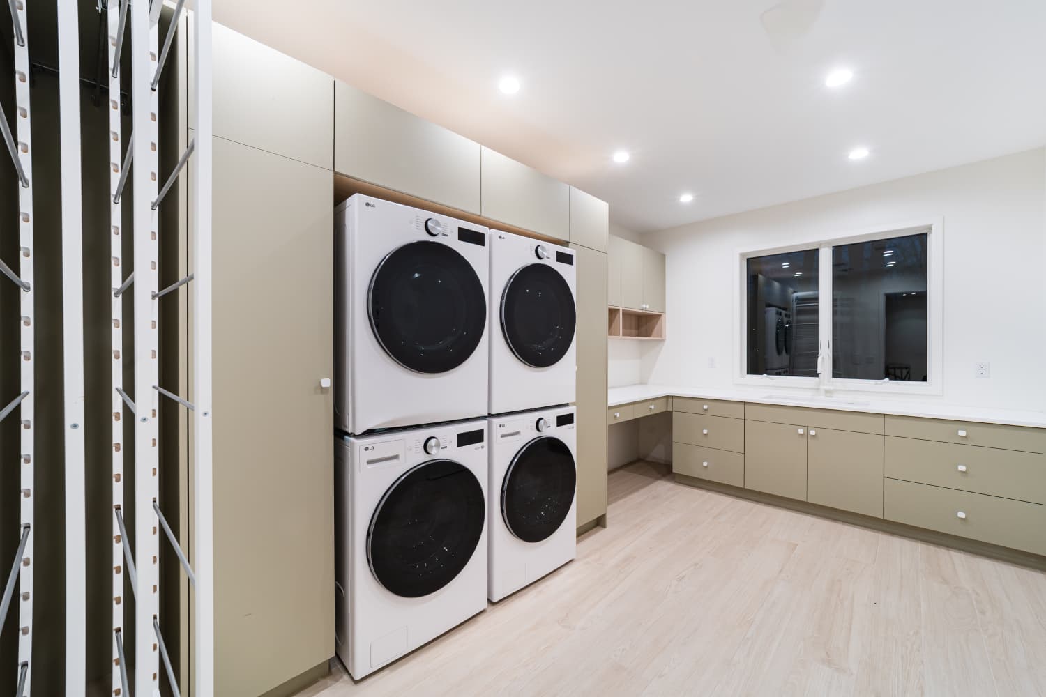Another angle of the laundry room with four stacked machines and sage cabinets
